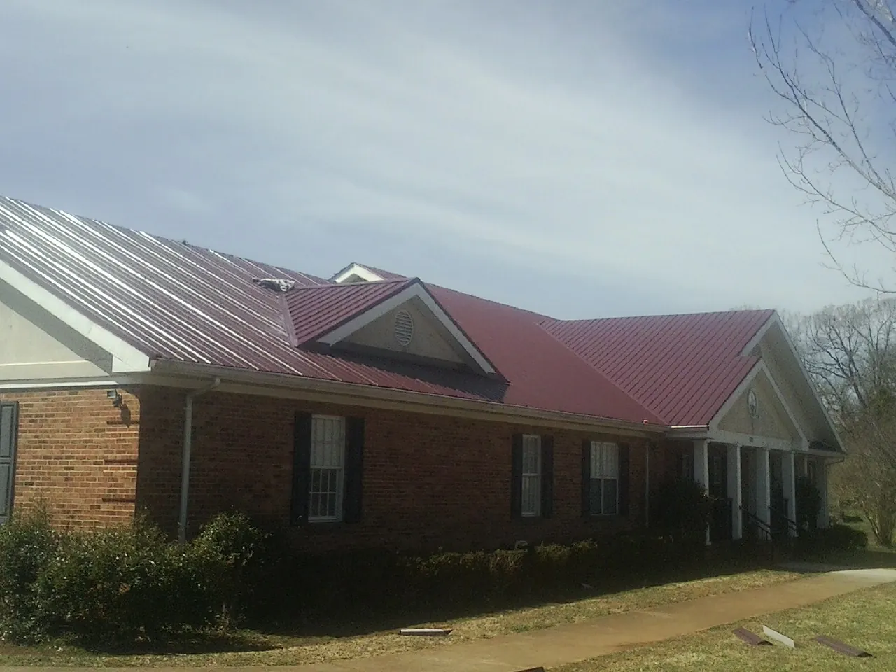Red metal roof with gabled entries on a long brick building, from a Hail Damage Roof Repair job in Collinwood