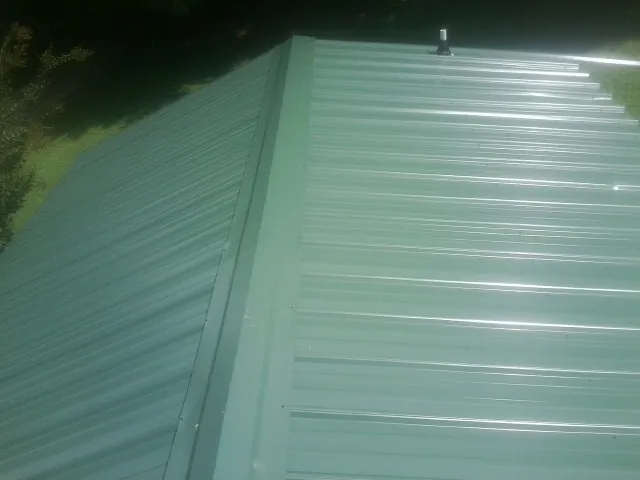 New green metal panels meeting at the ridge of a roof — Flat Roof Repair work by our crew in Collinwood