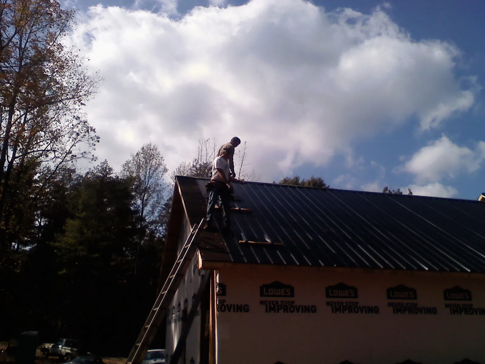 Roofer fastening dark metal panels high against a cloudy sky, from a Roof Inspection job in Collinwood