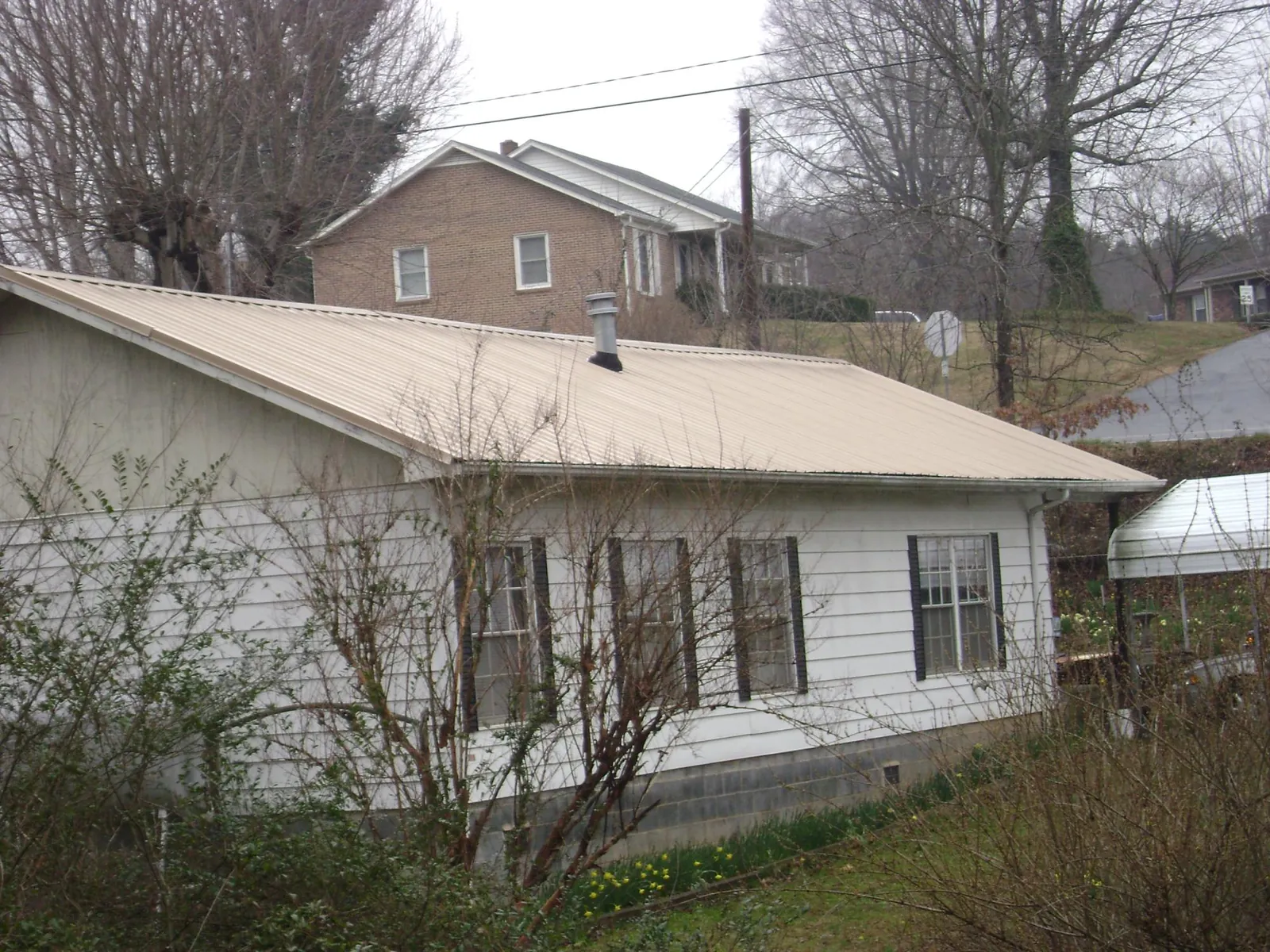 Tan metal roof on a white sided house set into a hillside — Commercial Roofing by Roofing Brothers in Collinwood